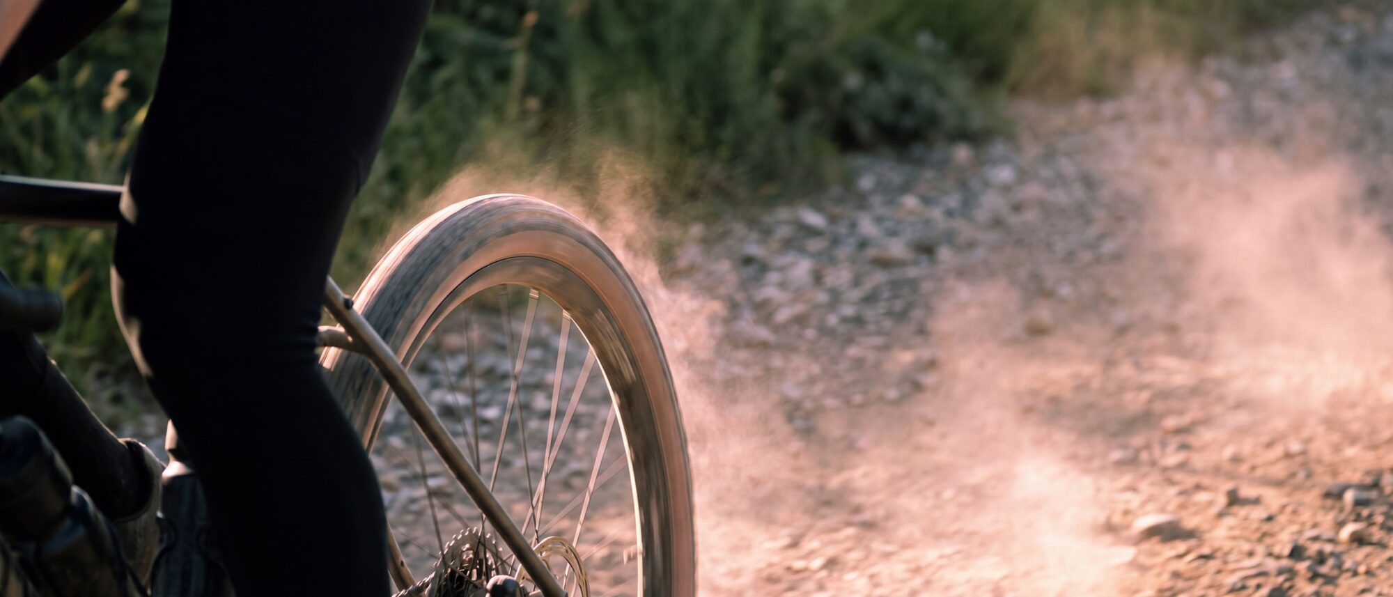 Ruota e gamba di un ciclista su uno sterrato asciutto, con la polvere sollevata dal passaggio