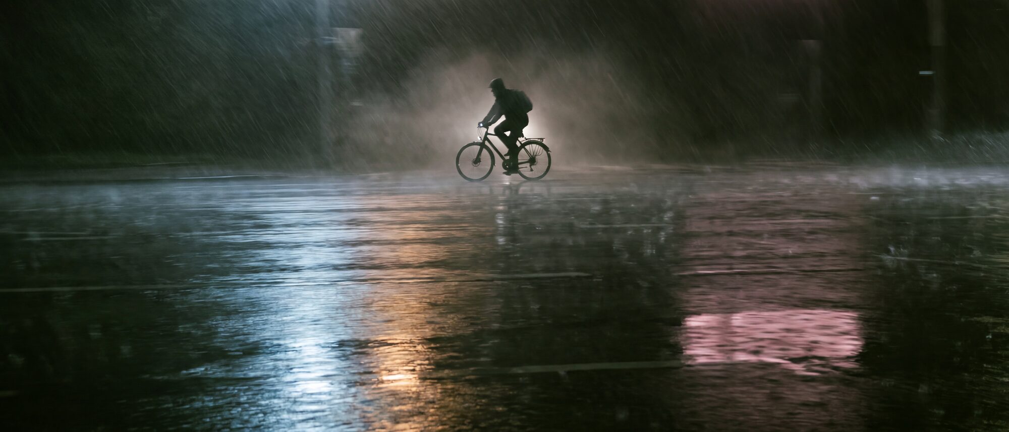 Asfalto bagnato sotto la pioggia con i riflessi delle luci e una bicicletta in controluce